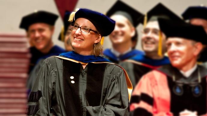 Jen 马修斯 in a cap and gown, smiling, surrounded by other professors