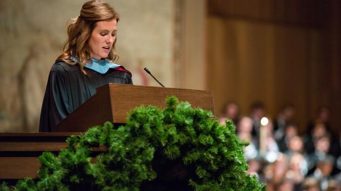 Jamie Thompson speaks at a podium wearing regalia