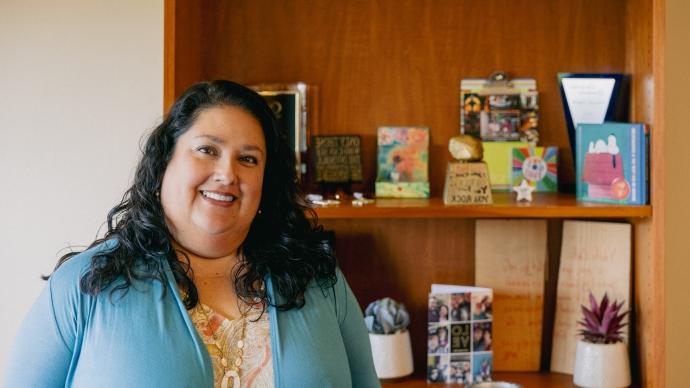 Catherine Fragoso stands in front of a bookshelf with family photos