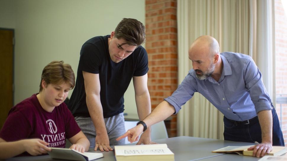 chad spigel pointing at a book next to two students