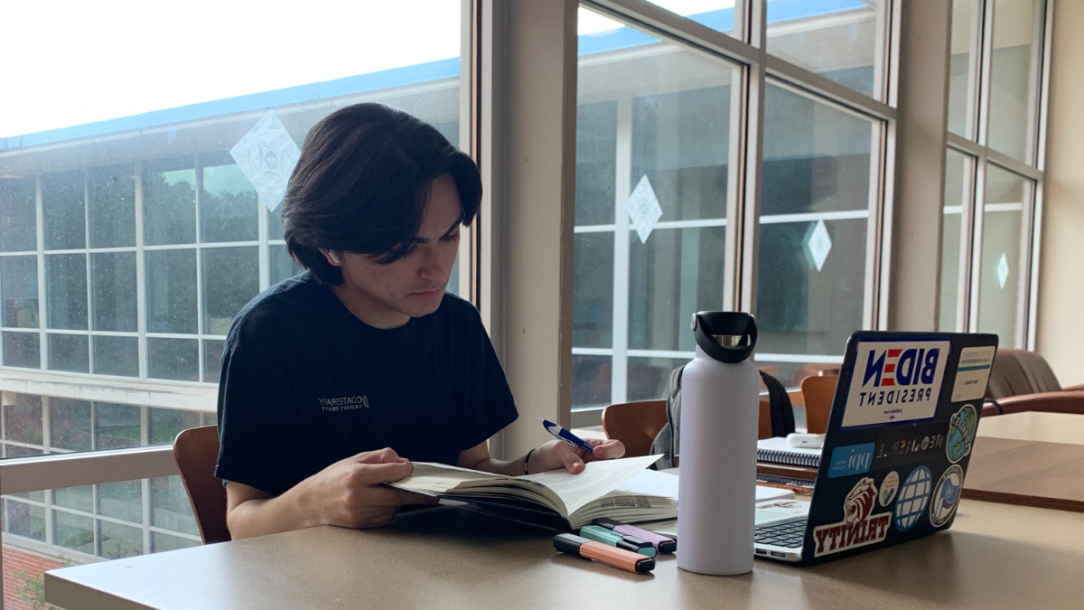 Benjamin Falcon sits at a table with his laptop, reading through a book